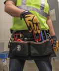 Worker wearing Heavy Duty Tool Apron With Reinforced Bottoms And Four Pockets For Hand Tools Tape Thong And Pencil Pockets Adjustable Belt Fits 32 To 53 Inch Waists Built For Rugged Work And Ready For Everyday Pro Use filled with tools in workshop setting.