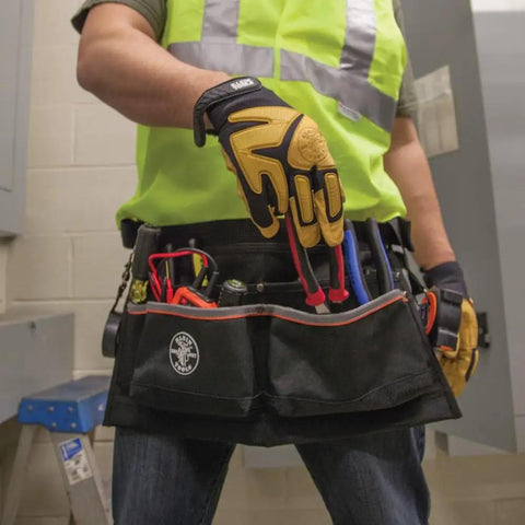 Worker wearing Heavy Duty Tool Apron With Reinforced Bottoms And Four Pockets For Hand Tools Tape Thong And Pencil Pockets Adjustable Belt Fits 32 To 53 Inch Waists Built For Rugged Work And Ready For Everyday Pro Use filled with tools in workshop setting.