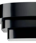 One Light Louvered Wall Sconce Light Fixture In Black Finish, Modern Design For Entryway Hallway Foyer Bedroom And Living Room, Tri Band Louvered Shade That Glows From The Top, Seven Inch Tall close-up showing matte black louvered bands.