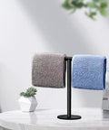 Hand Towel Holder Stand For Bathroom Vanity Countertop Matte Black Finish Free Standing Design Space Saving Movable T Shape Towel Bar Rack For Kitchen And Bath with folded towels on a table.