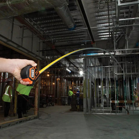 Person holding Heavy-Duty Tape Measure With Nylon-Coated Blade, 25-Foot Reach in construction site, demonstrating curved extension