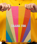 Person holding Rainbow Color Waterproof Poly Mailer Bags 100 Count Self Sealing Shipping Envelopes with 'Thank You' design.