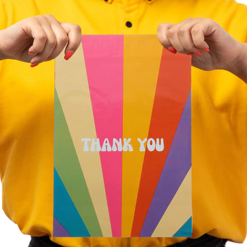 Person holding Rainbow Color Waterproof Poly Mailer Bags 100 Count Self Sealing Shipping Envelopes with 'Thank You' design.