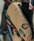 Person inserting phone into Toprock Frame Bag For Road And Gravel Cycling Water Resistant Cordura 1000D With Durable YKK Aquaguard Zipper Top Tube Frame Storage For Daily Essentials And Bikepacking Coyote Color 1 Liter attached to bike