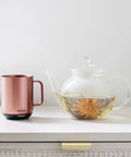 Renewed 6 Oz Smart Heated Coffee Mug With App Precision Temp Control And Solid Battery Life Keeps Your Favorite Brew Piping Hot And Ready For All Day Sipping Sessions next to a glass teapot.