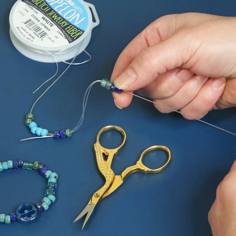 Hook Eye Needle For Beading 10 Inch Long Extra Fine Bead Stringing Tool in use with beads, thread, and a pair of scissors.