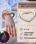 Gold Finish 22K Purse Hook For Table, Heart Shaped Portable Handbag Holder For Desk Travel Cafe And Office displayed on wrist