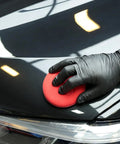 Applying polish with a 10 Pack Foam Wax Applicator Pads For Car Detailing, 4 Inch Red Hand Wax Pads on a car surface, close-up.