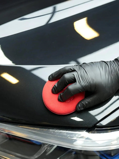Applying polish with a 10 Pack Foam Wax Applicator Pads For Car Detailing, 4 Inch Red Hand Wax Pads on a car surface, close-up.