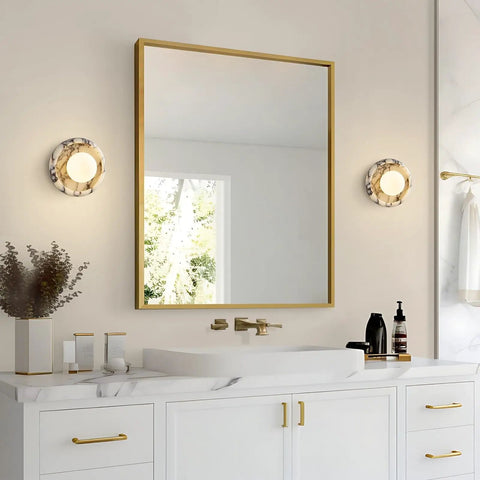 Alabaster Wall Sconce, 7.5" Natural Marble Wall Lamp with Milk Glass Shade beside a round mirror in a modern bathroom.