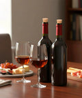 Two wine bottles with Natural Cork Stoppers Set For Glass Bottles 36 Pieces With Six Handy Sizes on a table next to wine glasses.