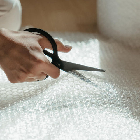 Thickened LDPE Bubble Wrap Roll for Moving and Shipping being cut with scissors, showing eco-friendly packing material detail.