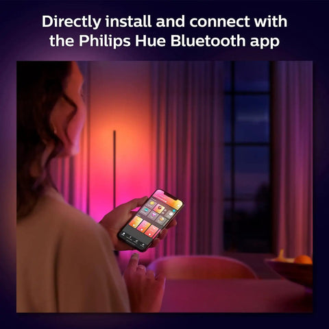 Person using smartphone to control Indoor 3-Foot Smart LED Light Strip Extension with Hue app, soft colorful glow indoors