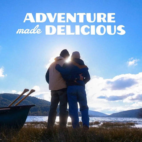 Two people embracing near a canoe by a lake with "Adventure made delicious" text above.