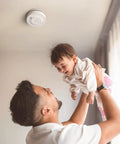 Father holding baby with No Sweat Ten Year Battery Photoelectric Smoke Detector With Cooking Fume Blocker above them.