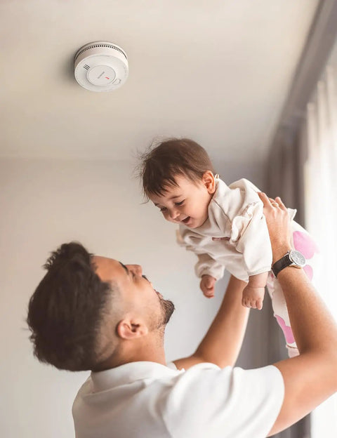 Father holding baby with No Sweat Ten Year Battery Photoelectric Smoke Detector With Cooking Fume Blocker above them.