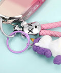 Close-up of a silver keyring with a toy and purple unicorn charm against a light blue background.