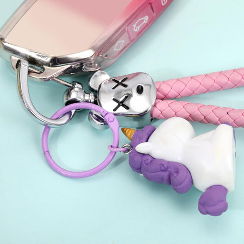 Close-up of a silver keyring with a toy and purple unicorn charm against a light blue background.