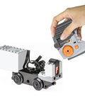 Hand holding remote with 36 Pcs Power Functions Motor Set for STEM Building Blocks, including battery boxes, motors, and wheels.