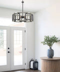 Rustic 24 Inch 5 Light Farmhouse Chandelier With Adjustable Hanging Height In Gray Oak Wood Look And Sandblasted Black Finish, Open Geometric Frame above entryway.
