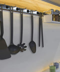 Kitchen utensils hanging on a metal rack under a shelf, wall-mounted spice jars, wooden spatula and ladle visible.