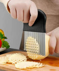 Crinkle cutter knife with black handle and stainless steel ribbed blades slicing a potato into crinkle fries.