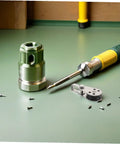 Assorted tool parts and screws on green surface with screwdriver and metal socket adapter.