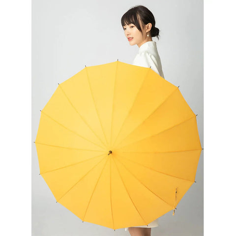 Woman holding yellow umbrella with long handle and wide coverage against plain background