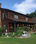 Top Shelf Heavy Duty Oil Based Wood Stain For Exterior Decks Fences Siding Logs Featuring Knockout UV Shielding And Deep Soak Water Repellent Formula In Easy Roll Semi Transparent Rustic Brown Covers Large Patios applied to a log cabin home with flower gardens.