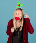 Person holding festive props in front of blue background, wearing red cardigan and black top, playful holiday expression.