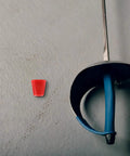 Red plastic connector next to a fencing saber, part of the Built To Last Fencing Replacement Kit With Stainless Steel And Plastic Connectors For Sabers And Accessories, Versatile Hardware Repair Tool To Keep Your Gear Safe, Stable And Ready For Action.