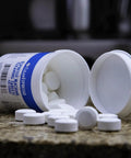 Front view of CleanEspresso cleaning tablets bottle spilled on countertop with white round tablets