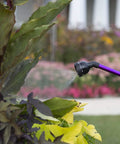 Kaleidoscope Rain Wand 16-Inch Touch-N-Flow with trigger gently watering garden plants with soft spray pattern, purple handle visible.