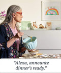 Hella Compact Smart Speaker With Alexa Built In Drops Kickass Soundwaves Smooth For Cozy Rooms Stereo Pairing Ready Charcoal Shell, woman using speaker in kitchen.