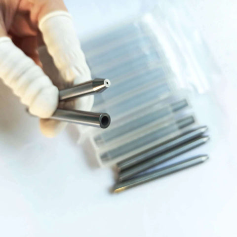 Close-up of stainless steel abrasive water jet nozzle tips held by gloved hand; six nozzles visible in background