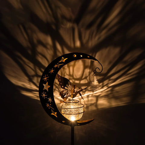 Moon Fairy Garden Solar Light Glass Globe With Angel Decor casting shadows, waterproof warm LED pathway light at night.