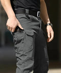 Person wearing dark gray mens tactical cargo pants with stretch waterproof fabric, showcasing multi-pocket design, no belt.