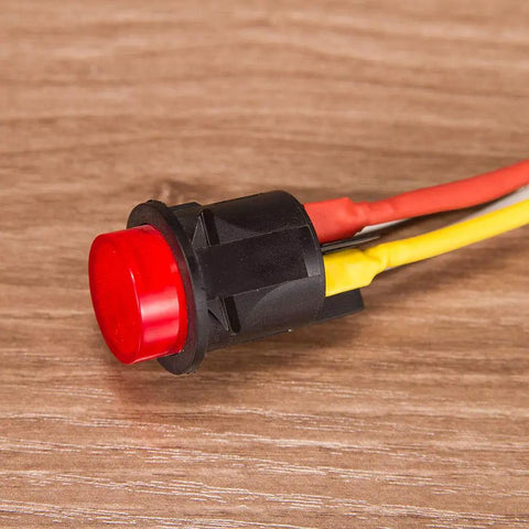 Close-up of a red push button switch with attached insulated wires on a wooden surface.