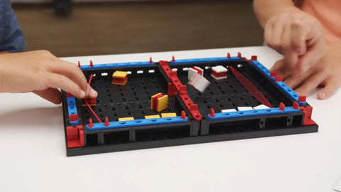 Slide Battle Building Kit With 102 Components For Big Kids And Adults Who Love To Build And Create, Ages 7 And Up, A Smart Expansion For Your Build Your Own Game Set, Perfect For Get Your Game On Competitive Play And Brain Boosting Fun. hands playing on a tabletop build game board with plastic pieces