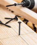 Heavy Duty Workhorse 6 X 1 1/4 Fine Thread Drywall Screw self-tapping in wood, showcasing solid black phosphate coating.