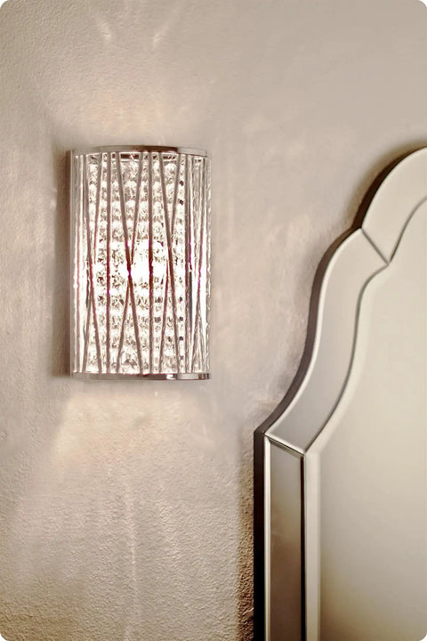 Wall-mounted light fixture with textured glass and metal design next to a bed headboard.
