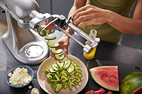 Person using the 7 Blade Spiralizer Plus With Peel Core And Slice Attachment For Stand Mixer Power Hub to spiralize cucumber.
