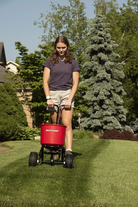 Person using 2600A-PLUS Fertilizer Spreader with 40Lb hopper and beefy all terrain pneumatic tires on a lawn.