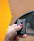 Hand holding remote for Weatherproof Outdoor Outlet Switch With Wireless Remote Controller next to car mirror