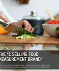 Person chopping green onions with knife, tomatoes and peppers nearby, kitchen pot in background, text about food measurement brand.