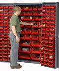Man organizing items in Straight Up Heavy Duty Storage Bin Cabinet With 132 Red Plastic Organizers Featuring Slick Louvered Doors Swinging Wide Open For Quick Workshop And Garage Setup.