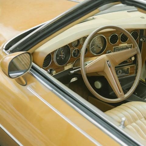 Automotive interior view of a vintage tan car with a wood‑grain dashboard and beige steering wheel