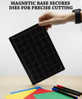 Person holding Pro Grade Magnetic Die Cutting Shim 9x6 Inch with Grid, shown with colored paper and pens for crafting.