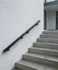 Heavy Gauge Wall Mount Stair Handrail In Matte Black Stainless Steel For Indoor Outdoor Stairs on concrete steps with rain.