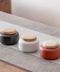 Handcrafted Ceramic Tea Canisters With Airtight Wooden Lids Keep Your Daily Stash Locked In This Rock Solid Porcelain Storage Set Of Four For Modern Home Kitchens. Three jars in black, white, and red on a table.